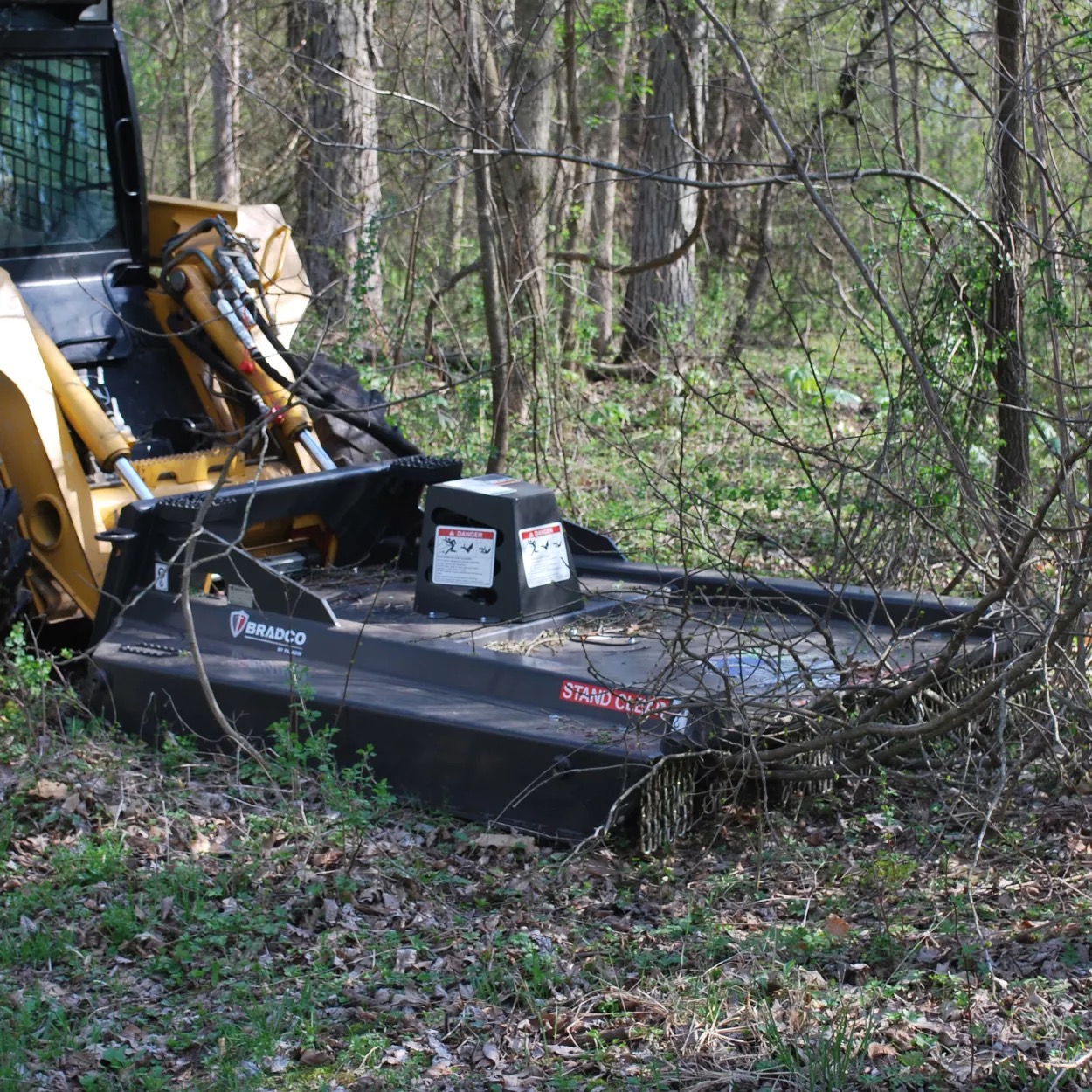 Brush hog attachment cutting field-edge vegetation and light brush